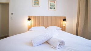 Une chambre d’hôtel avec un lit, deux lampes fixées au mur et deux tableaux encadrés accrochés au mur.