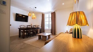 Un salon comprenant un canapé, une table basse, un téléviseur fixé au mur et un coin repas avec des chaises et une table.