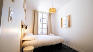 A hotel room with a bed, bedside table, lamp, window with curtains, and a wall-mounted mirror. - La Maison Momiji - Elegance and the Art of Living (Tours)
