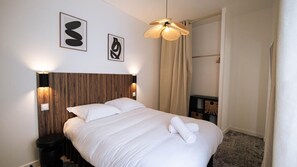 A hotel room with a wooden headboard, a bed with white linens, two wall-mounted lights, a ceiling fan, and a small bedside table with a lamp. - La Maison Momiji - Elegance and the Art of Living (Tours)