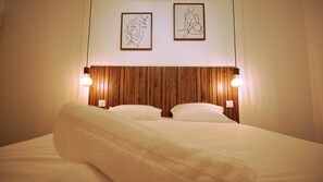 Hotellihuone, jossa on puinen päätyseinä, kaksi yöpöytävalaisinta ja taideteoksia seinällä.