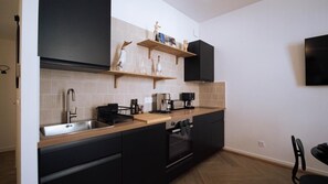 Moderni keittiö, jossa on mustat kaapit, ruostumattomasta teräksestä valmistettu allas ja sisäänrakennettu uuni.