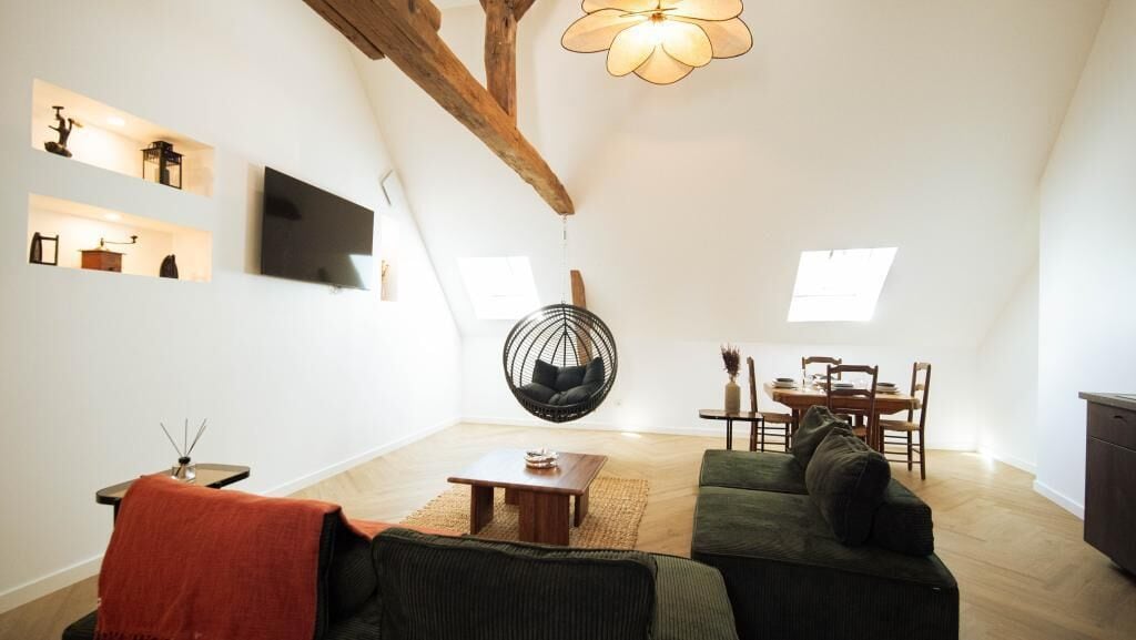 Una sala de estar moderna con un sillón colgante, un sofá, una mesa de comedor y un televisor montado en la pared.