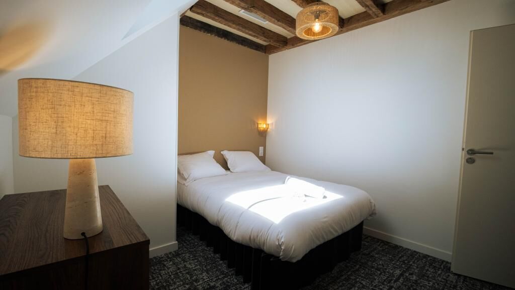 A bedroom with a bed, a bedside lamp, a wall-mounted light, and a door.