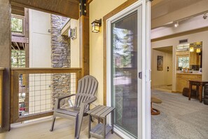 Une terrasse en bois avec une chaise, un mur en pierre et une porte-fenêtre coulissante donnant sur un espace cuisine.