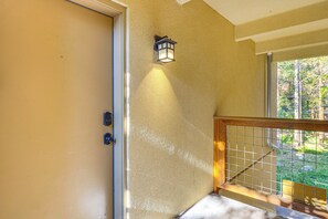 Un escalier avec un mur à texture, une porte avec une poignée et une fenêtre donnant sur des arbres.
