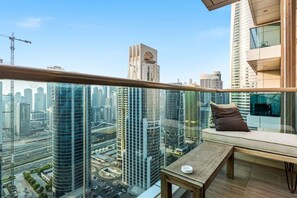 A high-rise building with a balcony featuring a wooden table and a cushioned seat, overlooking a cityscape with modern skyscrapers. - Relaxing City Escape in JLT (Dubai)