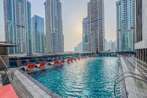 A swimming pool with red chairs and a view of high-rise buildings. - Relaxing City Escape in JLT (Dubai)