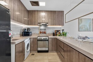 A modern kitchen with a built-in washing machine, a stove, and a microwave. - Relaxing City Escape in JLT (Dubai)