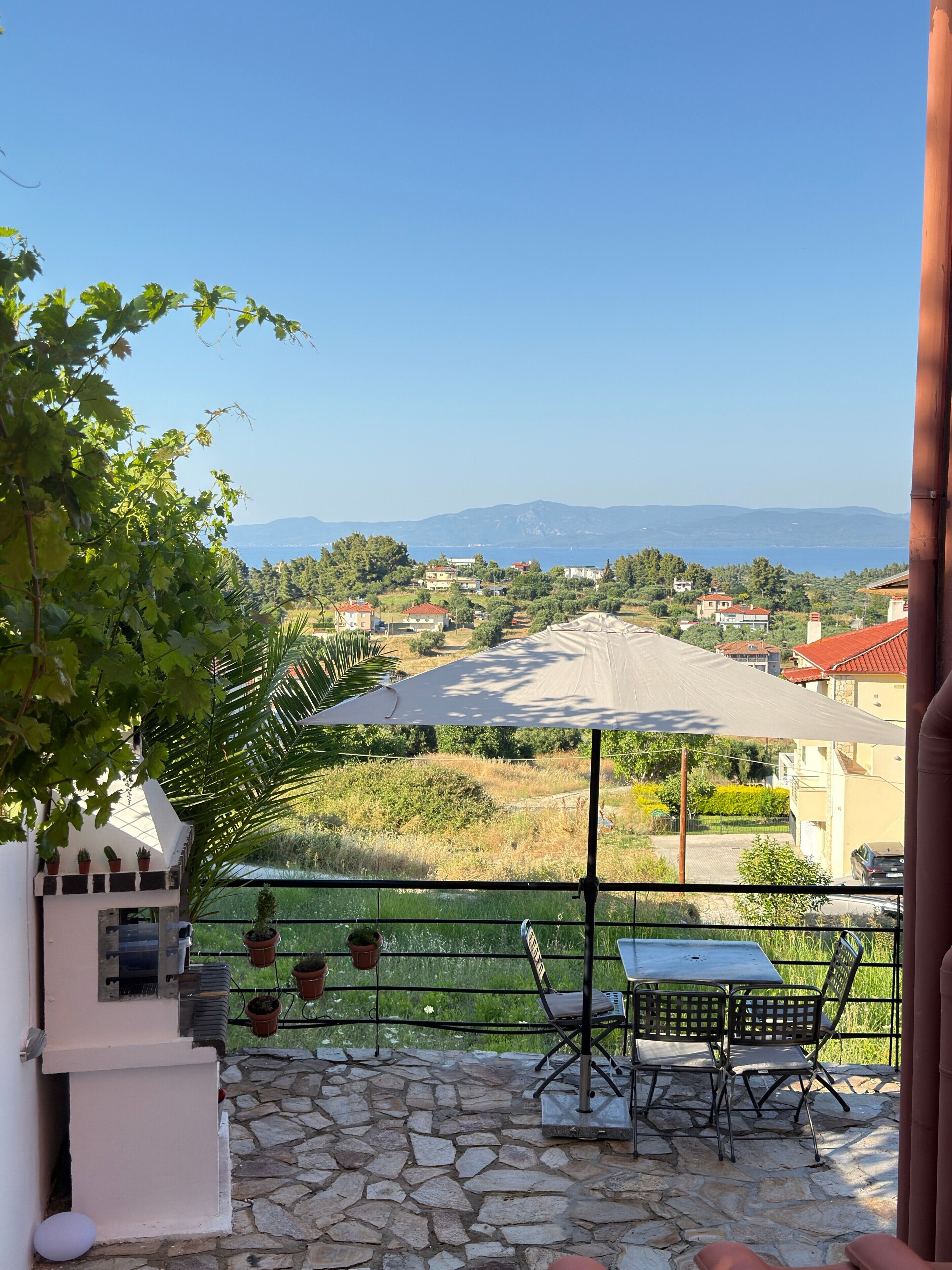 A patio with a table and chairs, a grill, and a view of a coastal town.