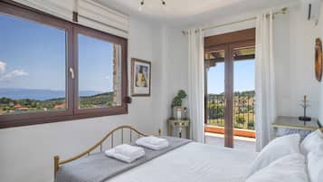A bedroom with a bed, a window, a door leading to a balcony, and a view of the landscape.