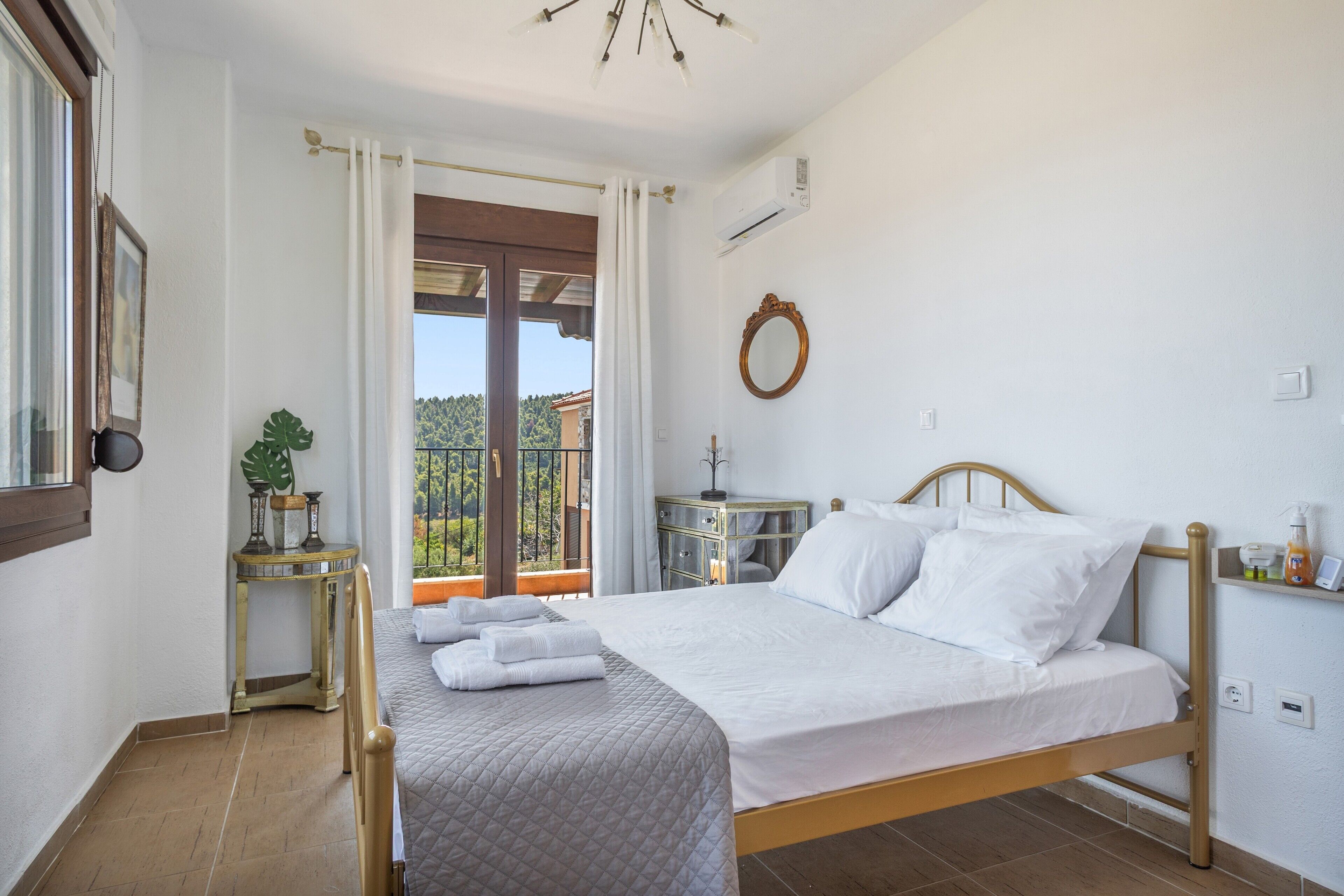 A bedroom with a bed, a bedside table, a mirror, and a view of the outdoors.