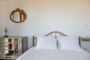 Un dormitorio con cama, mesita de noche, espejo y un interruptor de luz en la pared.