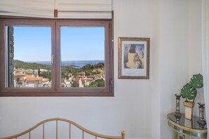 Una habitación con un ventanal grande que da a un pueblo costero, una obra de arte enmarcada en la pared y una pequeña mesa con adornos.