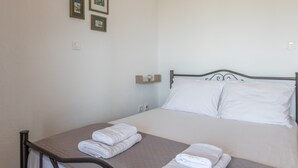 Una cama individual con estructura metálica y dos almohadas, una mesita de noche con lámpara, y una pared con tres cuadros enmarcados.