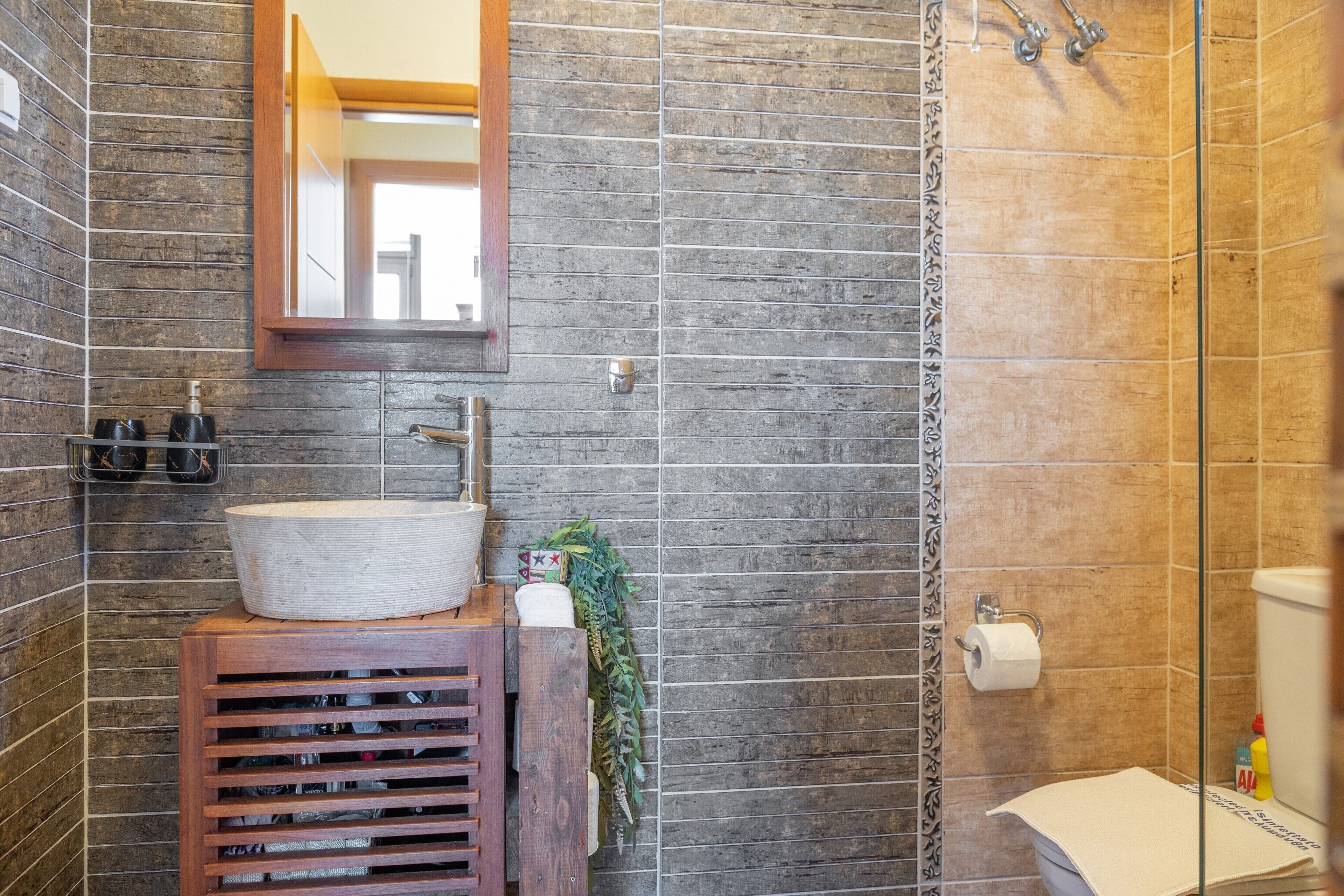 A bathroom with a wooden vanity, a mirror, a sink, and a shower area.