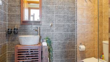 A bathroom with a wooden vanity, a mirror, a sink, and a shower area.