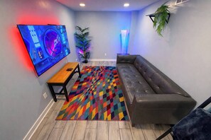 Ein modernes Wohnzimmer mit einer Ledersofa, einem Holztisch, einem bunten Teppich, einem Flachbildfernseher und einer Zimmerpflanze.