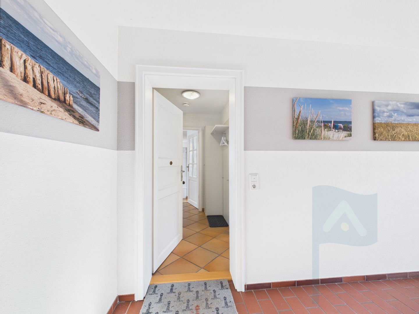 A hallway with a door leading to another room, a patterned rug, and wall-mounted pictures.