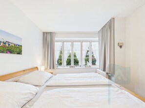 Habitació d'hotel amb dos llits, una finestra amb cortines, un quadre a la paret i una taula petita amb una làmpada.