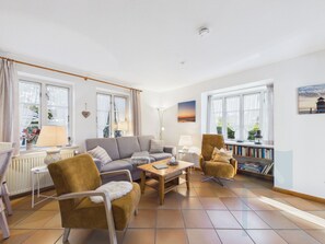 Ett väl upplyst vardagsrum med en soffa, fåtöljer, ett soffbord och en bokhylla.