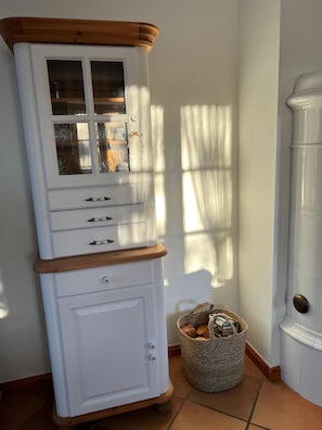 A white cabinet with multiple drawers and glass doors, a woven basket with items, and a wooden door frame. - Ingke Vacation Rental with a Fireplace – Family Vacations on Föhr - Boldixumer Straße (Wyk auf Föhr)