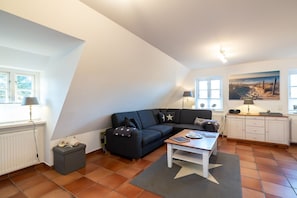 Ein Loft-Wohnraum mit schwarzem Sofa, einem Holztisch, einem Teppich mit Sternenmuster, einem weißen Schrank und einem Strandbild.