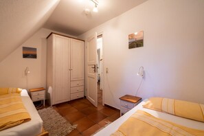 Ein Schlafzimmer mit zwei Betten, einem Kleiderschrank, einer Tür zu einem anderen Raum und einem kleinen Nachttisch.