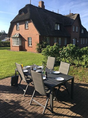 Ein Backsteinhaus mit Strohdach, einem gedeckten Tisch und Gartenstühlen.