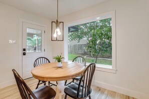 Un coin repas avec une table ronde en bois, quatre chaises, une plante en pot et une fenêtre donnant sur un jardin.