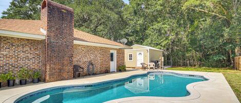 A backyard with a swimming pool, a brick house, and a wooden deck.