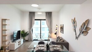 Una sala moderna con televisor de pantalla plana, un comedor con mesa de vidrio y un sofá.