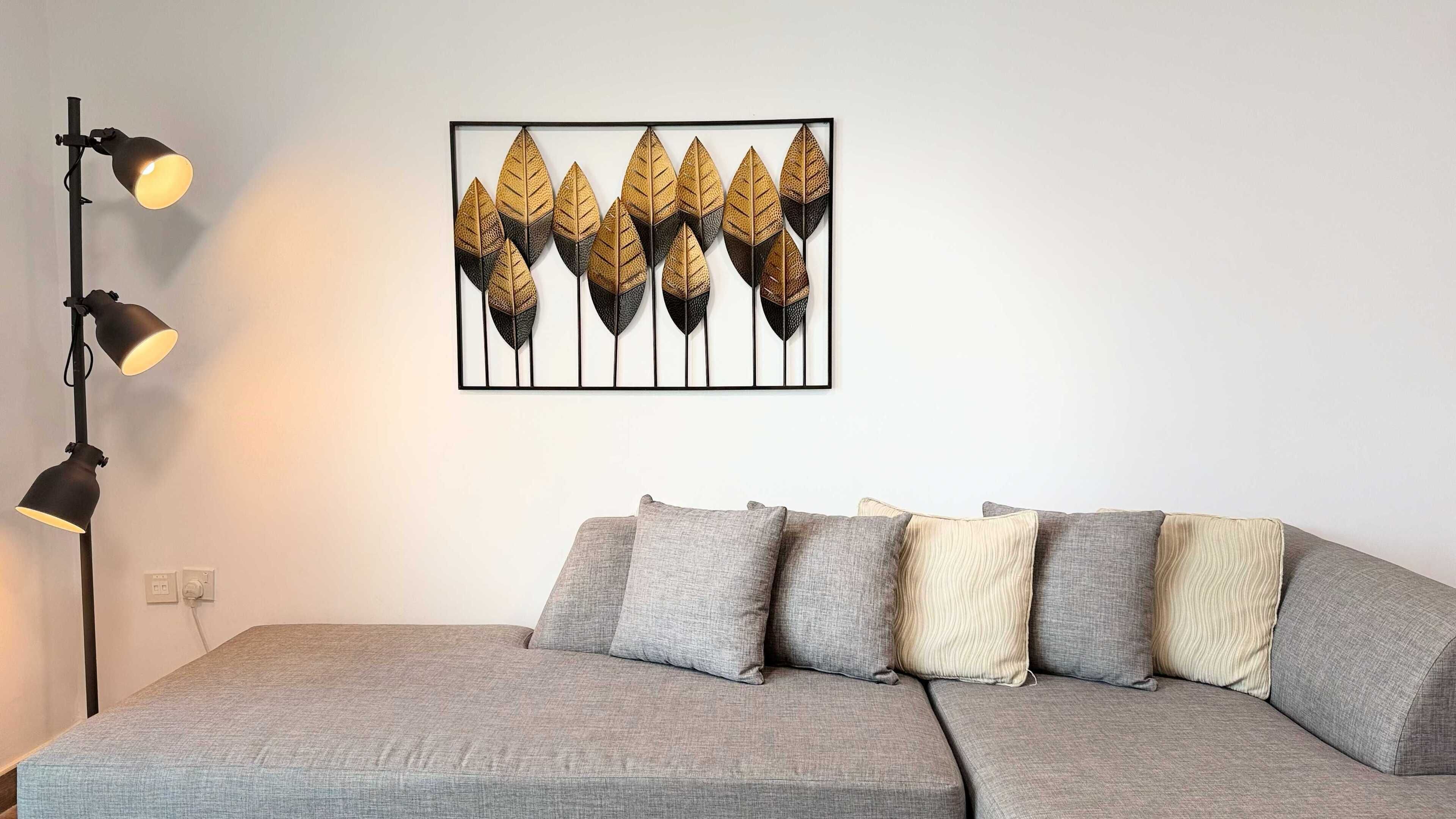 Une pièce avec un canapé gris, un lampadaire noir et une œuvre d’art encadrée représentant des feuilles, accrochée au mur.