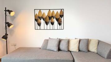 Une pièce avec un canapé gris, un lampadaire noir et une œuvre d’art encadrée représentant des feuilles, accrochée au mur.