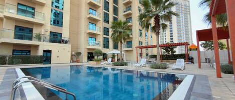A swimming pool with a clear blue water surface, surrounded by lounge chairs and palm trees.