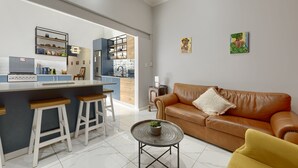 Uma cozinha moderna com uma ilha central, banquetas de bar, um sofá de couro marrom e uma mesa de centro redonda com uma planta.