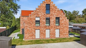 En moderne murbygning med skråt tag, flere vinduer og en lille balkon.