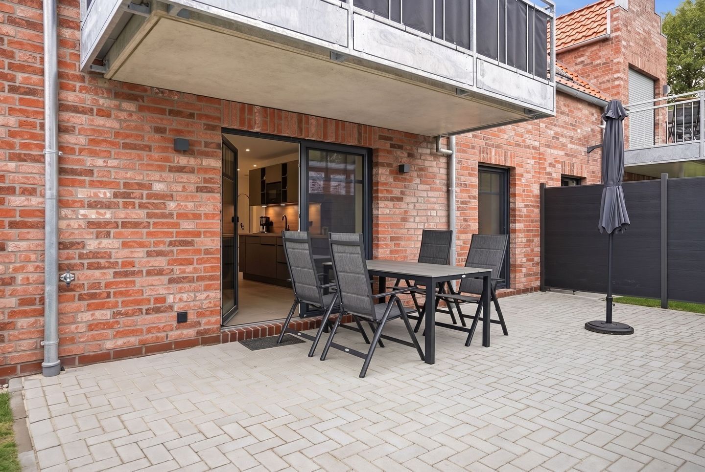 A brick building with a patio area featuring a table and chairs, a covered outdoor seating area, and a view of the interior kitchen.
