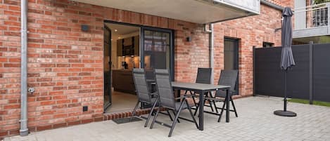 A brick building with a patio area featuring a table and chairs, a covered outdoor seating area, and a view of the interior kitchen.
