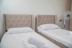 Two single beds with headboards, white bedding, and a standing fan.