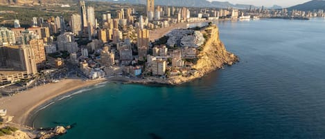 A coastal cityscape with high-rise buildings, a beach, and a mountainous backdrop.