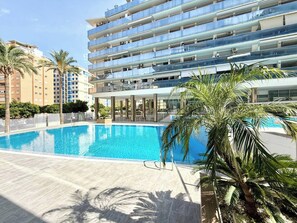 A modern hotel with a swimming pool, palm trees, and a multi-story building with balconies.
