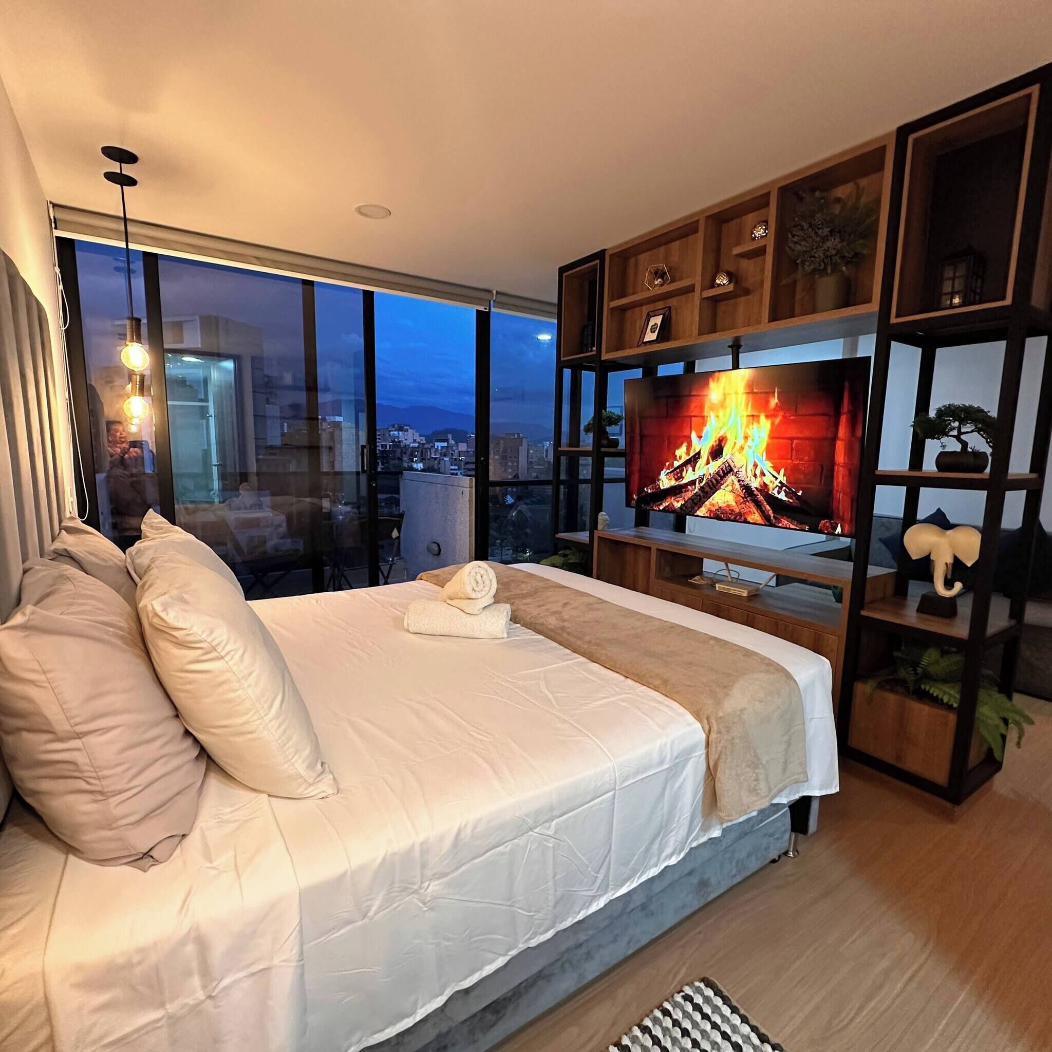 A modern bedroom with a large bed, a TV, and a city view.