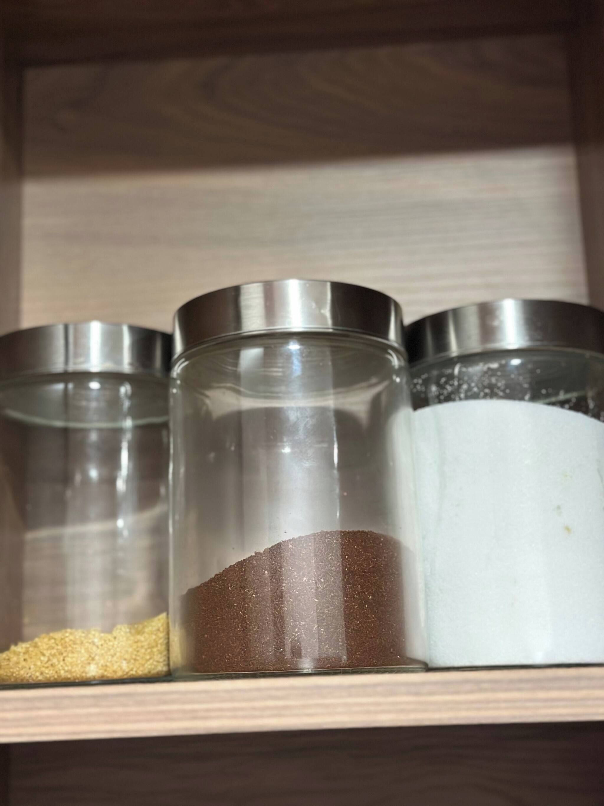 Tres recipientes de vidrio con tapas metálicas sobre un estante de madera.