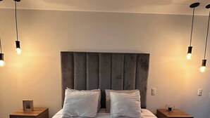 A neatly made bed with a grey headboard, two bedside tables with lamps, and a folded towel on the bed. - Premium Loft with AC  Panoramic View in Laureles (Medellín)