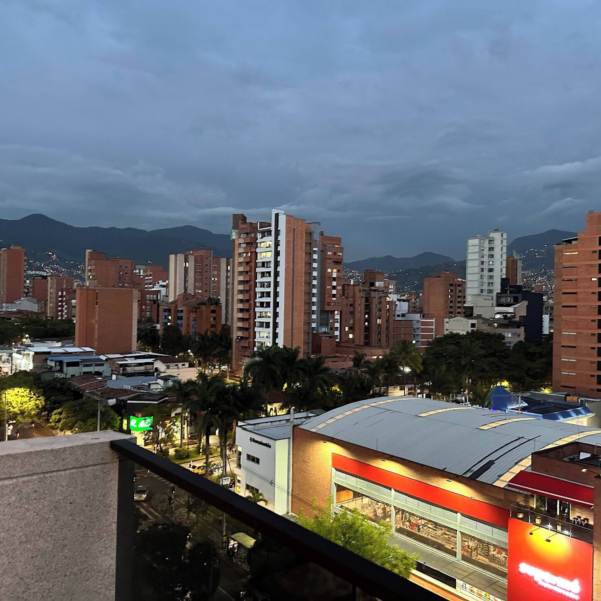 A cityscape with high-rise buildings, a shopping center, and mountains in the background.