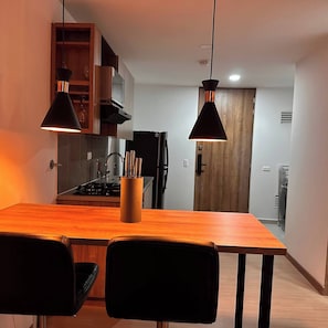 A modern kitchen with wooden cabinets, a black refrigerator, and a dining table with two chairs. - Premium Loft with AC  Panoramic View in Laureles (Medellín)