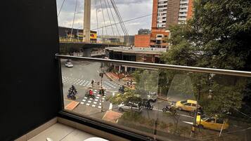 A balcony with two white chairs, a view of a busy street with vehicles and pedestrians, and a large bridge in the background.