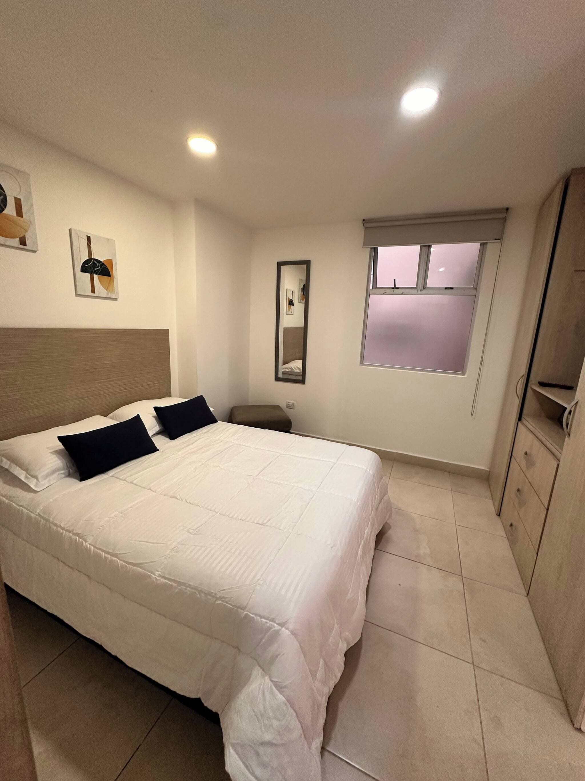 A bedroom with a bed, a nightstand, a mirror, a window, and a wardrobe.