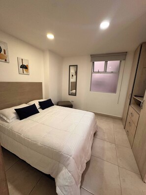 Un dormitorio con cama, mesita de noche, espejo, ventana y armario.